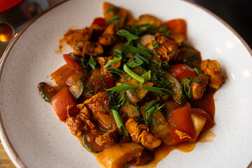 Deep-fried chicken dish with colorful vegetables, including bell peppers, onions and herbs. The dish is decorated with fresh green onions.
