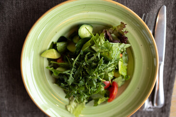 Fresh vegetable salad in a bowl of greens. The salad includes a variety of leafy greens, cucumbers and tomatoes. The dish is decorated in a simple rustic style.