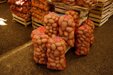 Fresh potatoes packed in red mesh bags stacked at a market. Concept of agriculture, harvest, and organic food trade