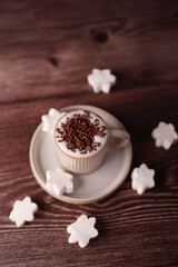 cup of frothy hot chocolate adorned with sprinkles surrounded by marshmallow snowflakes on dark wood surface, evoking a cozy and wintery atmosphere, mocha, satisfying, holidaytime, aesthetic, visual