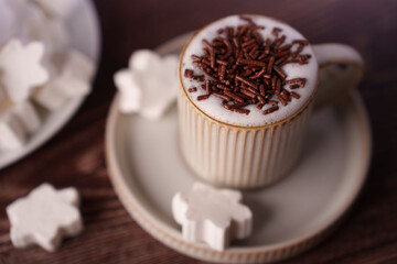 cozy hot chocolate in a ribbed mug topped with chocolate sprinkles and surrounded by marshmallow shapes on a wooden table creating a warm, inviting, sweet atmosphere, culinary, composition