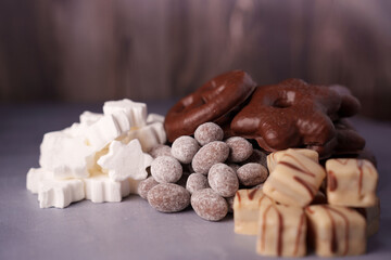 assortment of festive cookies and candies featuring chocolate pretzels, sugar-coated almonds, star-shaped marshmallows, and frosted square confections on a textured surface, layered, indulgent