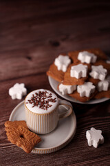 cozy wooden table setting with a warm cup of cappuccino topped with chocolate sprinkles, accompanied by decorative cookies and stacked star-shaped marshmallows on a rustic plate, snacktime, setting