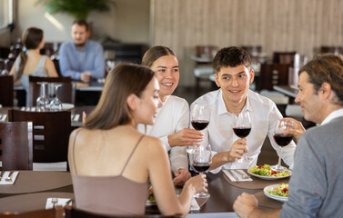Two couples of men and women drinking eating and talking in restaurant