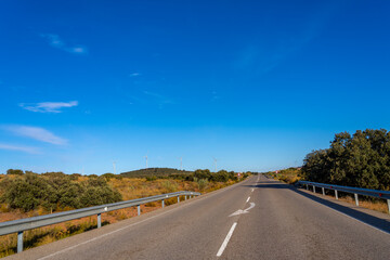 Fototapeta premium Open road with wind turbines under a clear blue sky.
