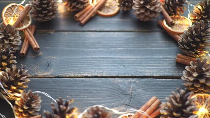 Cozy holiday background frame with pine cones, cinnamon, dried oranges and glowing lights on a rustic wooden table - Powered by Adobe