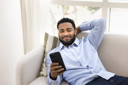 Guy resting lying on comfortable sofa at home with smartphone - Powered by Adobe