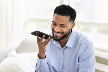 Young African man smile while talk on speakerphone