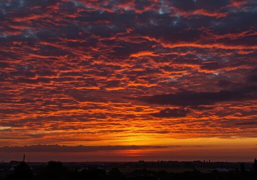 Dramatic sunrise lighting paints the heavy, textured clouds with fiery colors, creating a vibrant, peaceful morning sky scene above the horizon ,peaceful ,orange ,dramatic