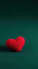 Fototapeta premium Handmade red knitted wool heart resting on a vibrant emerald green textured fabric surface, symbolizing affection and warmth ,valentines ,holiday ,close