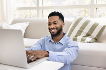 Fototapeta premium Smiling African man typing on laptop keyboard