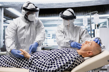 Doctors team in hazmat suits examining patient with infection symptoms in a secure laboratory,...