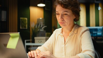 Female manager engaged in writing notes for a presentation on her laptop, extracting essential...