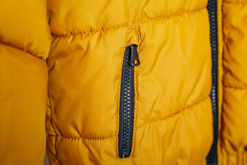 Close-up of a yellow winter jacket with a black zipper, showing fabric texture and stitching detail.