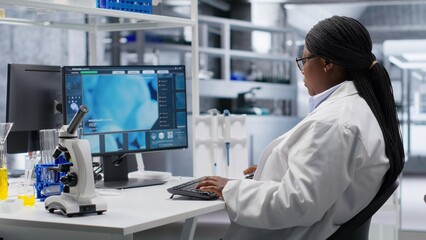 Black female chemistry expert opening laboratory software on pc and reviewing experiment data,...