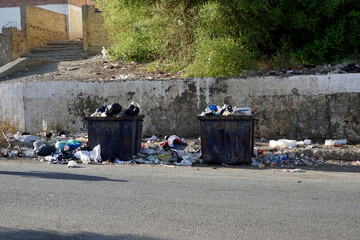 Overfilled garbage bins overflowing onto dusty curb