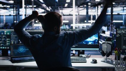 Overjoyed data center engineer dancing on chair after managing to analyze datasets using machine...