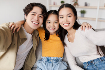 Obraz premium Two young adults and a girl pose closely together in a bright living room, smiling at the camera. They seem happy and relaxed while enjoying their time together.