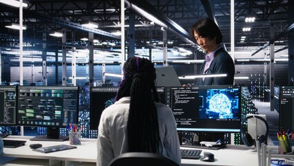 Team leader supervising technicians in server room using AI to review infrastructure diagnostics. Asian man in data center analyzing performance of workers using artificial intelligence, camera A