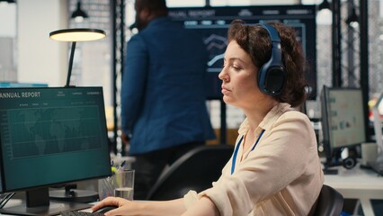 Young businesswoman focused on a podcast while she resolves office tasks, monitoring insights or...