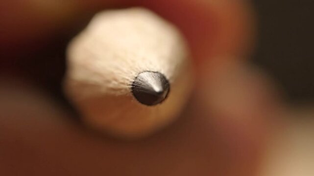 A close-up view of a pencil tip with a sharpened graphite point, blurred background