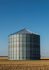 Massive cylindrical metal grain bin stands prominently in a rural field under a clear blue sky, illustrating large-scale agricultural storage ,agriculture ,galvanized ,feed