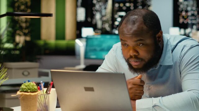 African american guy after hours feeling weary and overwhelmed, pushing limits despite clear signs of burnout. Workplace challenges and stress bring discomfort due to overtime. Camera B.