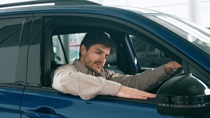 A man sits inside a blue car at an auto salon, deep in thought about buying, leasing, or renting options. The lighting is bright, highlighting his focus on the vehicle.