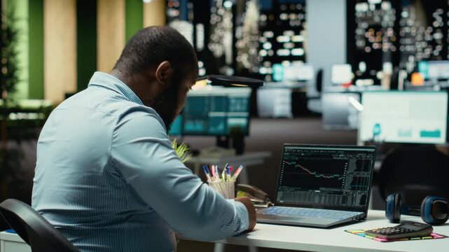 Worried finance advisor seeing the forex trends downward and losing money, concerned about failure and bankruptcy late at night. Frustrated sad person being displeased and stressed. Camera B.