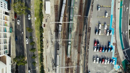 Train tracks intersecting roads with vehicles parked nearby in a bustling urban setting during daylight