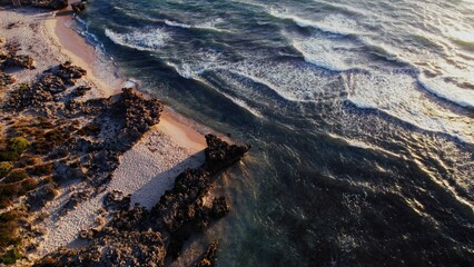 Coastline with sandy beach and rocky shoreline under a bright sky during sunset
