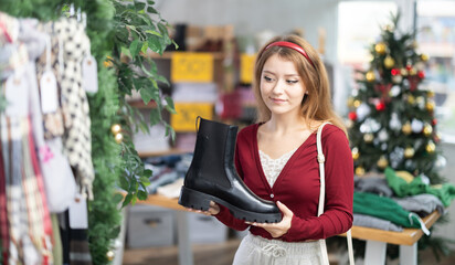Young woman standing in a Christmas shop on sale and choosing platform boots. Buying stylish winter shoes
