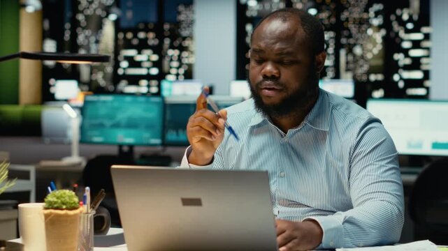 African american guy at the workspace sitting in deep concentration, pondering for a decision. Using laptop as he applies rational thinking and intuition for issue, mental haze. Camera B.