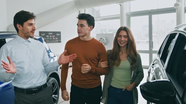A young couple interacts with a sales representative inside an auto salon, exploring options for buying, leasing, and renting vehicles. The atmosphere is bright and welcoming.