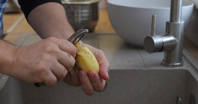 A man peels potatoes in the kitchen sink. Potato tubers for cooking.