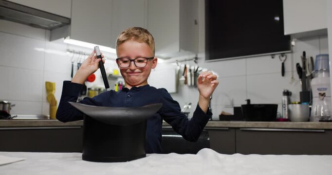 Smiling boy with glasses having fun in kitchen magic trick with black hat and a rabbit
