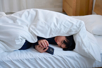 布団に包まってスマホを使う20代男性