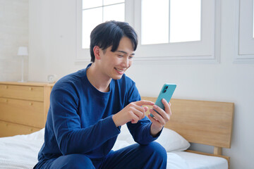 ベッドに座ってスマホを使う20代男性