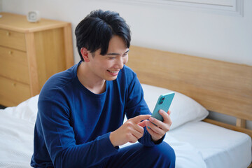 ベッドに座ってスマホを使う20代男性