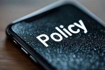 Close-up of a smartphone displaying the word “Policy” with a government building icon, symbolizing digital governance, regulation, and online administration.