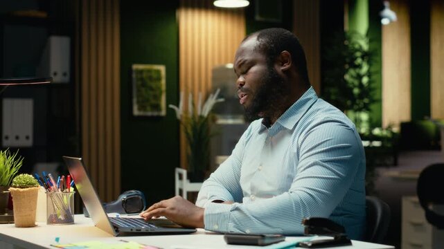 Angry african american guy getting mad and failing to finish tasks, dealing with burnout and mental exhaustion. Guy works after hours and facing weary challenges. Overwhelmed tensed male. Camera B.
