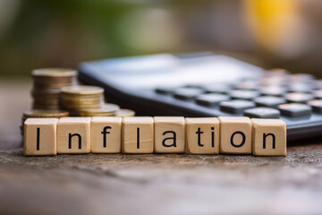 Wooden blocks spelling inflation with stacked coins and calculator in background symbolizing rising prices and financial analysis.