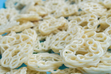 Close-up with selective focus on raw, uncooked Indonesian crackers (Krupuk) in a spiral, ring shape. Represents Asian snack food, abstract texture, culinary detail, and food preparation background.
