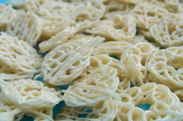 Close-up with selective focus on raw, uncooked Indonesian crackers (Krupuk) in a spiral, ring shape. Represents Asian snack food, abstract texture, culinary detail, and food preparation background.