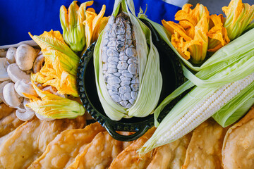 Variety of fresh Mexican ingredients (huitlacoche, squash blossom) next to quesadillas or empanadas ready to be tasted.