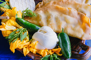 Molotes (fried Mexican street food) served with fresh cheese, squash blossoms, and jalapeño chiles on a rustic plate.