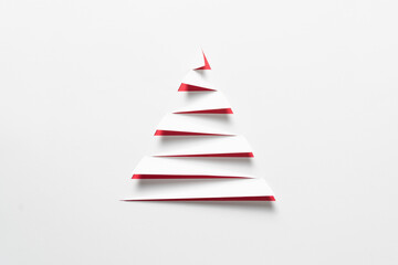 A minimalist white paper cut in a stepped, triangular shape to evoke a Christmas tree, with a striking red background showing through the cuts, for Christmas celebration or simple winter themes.