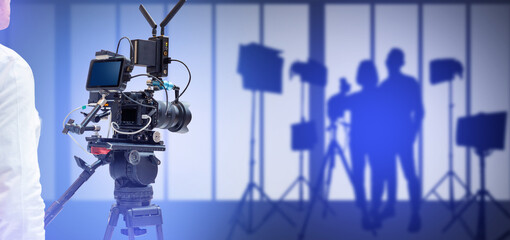 Film production with professional video camera on tripod, recording scene with crew silhouettes,...