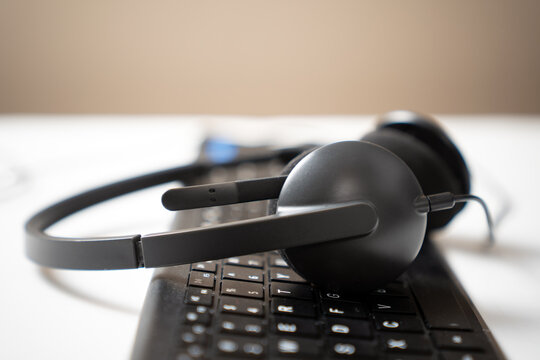 Low angle shot of a black headset with a microphone resting on a black computer keyboard. suggesting a theme of remote work, technical support, call centers, or online learning. - Powered by Adobe