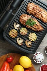 Electric grill with tasty chicken fillet, mushrooms, spices and products on wooden table, flat lay